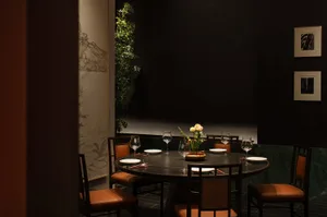 一張圓桌搭配座椅，中央擺放花卉，在燈光昏黃的工業風餐廳用餐區，搭配木質元素
