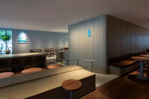現代極簡餐廳內部，擁有俐落金屬吧台、木質餐桌，以及混凝土牆面與藍色瓶飾