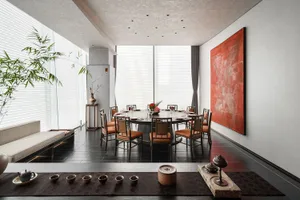A modern dining room with a large round table surrounded by chairs, set with plates, cutlery, and flowers. The room features 