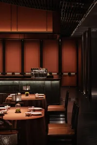Modern restaurant interior with brown leather chairs, black wood accents, and dark, moody lighting.
