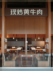 Modern restaurant interior with wooden tables, white chairs, and glass partitions.