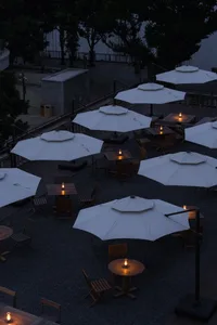 Outdoor seating arrangement of wooden tables and chairs under white umbrellas with candle lights.