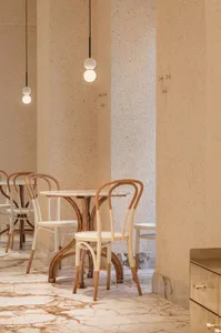 Minimalist restaurant interior with concrete walls, wooden dining chairs, and white pendant lights hanging above tables.
