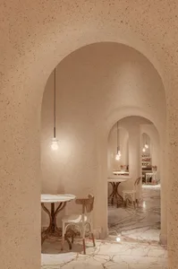 A modern restaurant interior with concrete walls and floor, featuring minimalist furniture and geometric light fixtures.