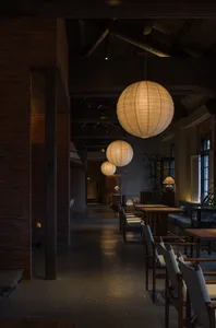 Industrial-style restaurant interior featuring hanging paper lanterns, wooden seating, and concrete flooring.