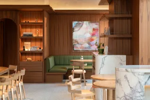 A modern restaurant interior with marble and wooden furniture, green leather seating, and abstract artwork on the wall.
