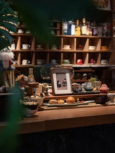 A cozy café scene featuring a display of ceramic and wooden items on shelves, with a framed picture of two people, and variou