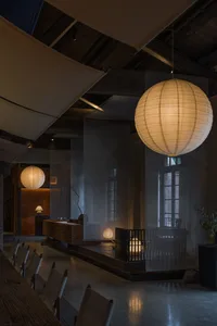 An interior space featuring minimalist design, with paper lanterns hanging from the ceiling and concrete furniture.