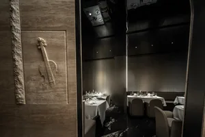 Modern restaurant interior with concrete walls and a violin wall art piece, featuring set dining tables and chairs.