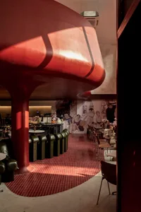 A modern cafe interior with a metallic red ceiling, round tables, and green leather seating