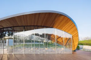 A modern wooden and glass cafe with a curved roof and outdoor seating area.