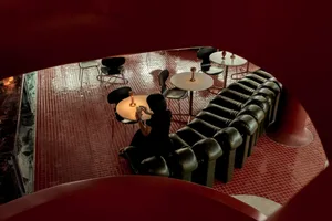 A modern cafeteria with black leather furniture and a metal floor, featuring a person sitting at a table with a drink.