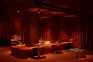 A modern nightclub interior featuring plush red velvet seating and illuminated tables, with a focus on the luxurious and eleg
