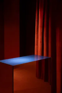 A dark room with red velvet curtains and a blue metallic table with blue lighting.