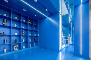 A minimalist blue coffee shop interior with metal shelves displaying coffee-making equipment and accessories.