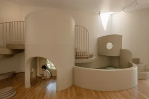 A modern, white playhouse with curved foam architecture designed for children's play, featuring a small window and steps.