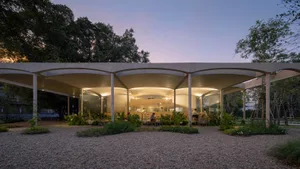 An illuminated restaurant with a modern design, featuring concrete structures and greenery.