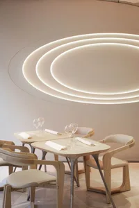 A modern restaurant interior with wooden tables and chairs, white walls, and circular light fixtures.