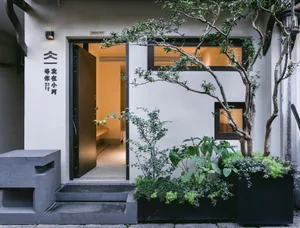 A minimalist house entrance featuring a concrete structure, open wooden door, and potted plants.