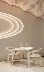 Modern restaurant interior with round wooden table, chairs, and illuminated architectural design on the ceiling.