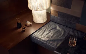 A modern bar counter with wooden and leather elements, featuring a lit lamp and a glass of drink.