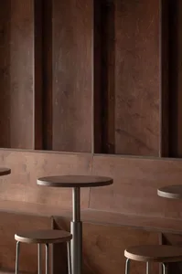 Modern café seating area featuring wooden stools and a round table with a concrete base, set against a wooden paneled wall.