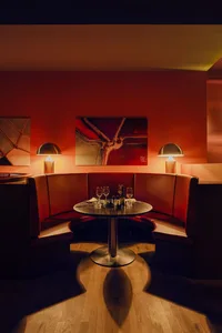 A cozy restaurant interior with red leather booths, a round table, and warm lighting.