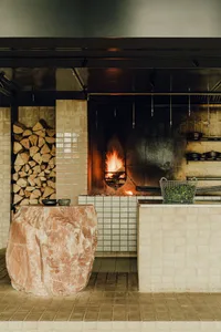 An industrial-style commercial kitchen with exposed brick walls and a firewood-stocked fireplace.