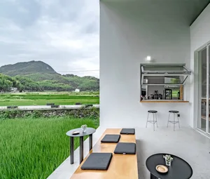 A minimalist outdoor living space featuring a sofa, coffee table, and a view of lush green fields and mountains.