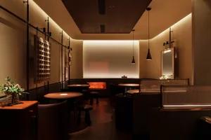 A minimalist restaurant interior with wooden tables, a glass partition, and warm lighting.