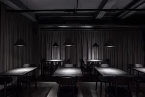 An empty minimalist-style restaurant interior with metal pendant lights and wooden tables.