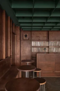 A modern cafe interior featuring wooden tables, stools, and shelving.