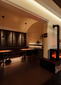 Industrial-style restaurant interior with wooden tables and chairs, firewood stove, and warm lighting.