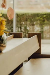 Close-up view of modern wooden interior table with a glass vase containing flowers and a window overlooking greenery in the b
