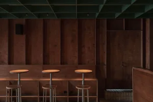 A minimalist bar area with a modern design featuring wooden and metallic surfaces and industrial stools.