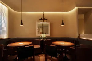 A modern restaurant dining room features round wooden tables with pendant lights, upholstered benches with leather accents, a