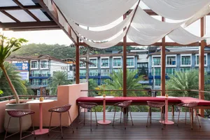 Modern industrial-style café with wooden tables and metal chairs, white fabric awning, and lush greenery surrounding the seat
