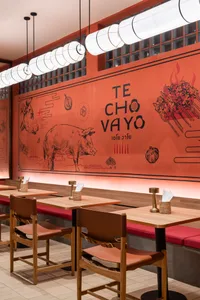 A modern restaurant interior featuring wooden tables, leather chairs, and wooden benches with a vibrant orange wall displayin