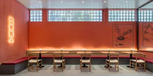 A modern restaurant interior with concrete walls, glass block windows, and wooden tables and chairs.