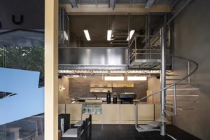 Industrial-style coffee shop with metallic counter, spiral staircase, and minimalist design elements.