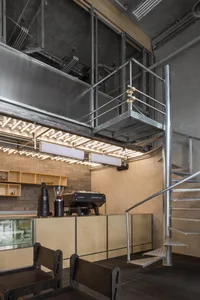 Modern coffee shop interior with steel staircase, wooden counter, and metal and glass walls.