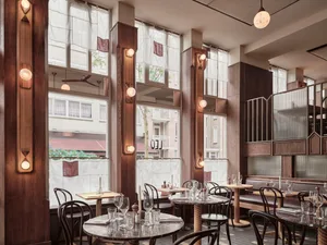 Industrial-style cafe interior with wooden tables and chairs, featuring high windows and natural light.