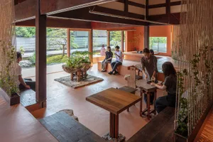 People enjoying a tea ceremony in a traditional Japanese tea house with wooden furniture and a natural garden view.
