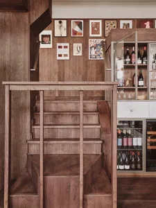 A wooden bar counter with a staircase leading to another level and a wine rack with bottles.