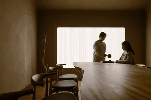 A minimalist tea ceremony room with a wooden table and a woman serving tea
