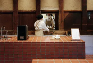 A café with a brick-tiled bar counter where two employees are interacting at a window.