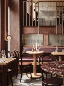 Modern restaurant interior with marble and wooden tables, glass wall partitions, and upholstered seating.