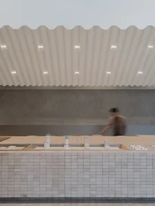 A minimalist coffee shop interior with a tiled counter and a corrugated ceiling.