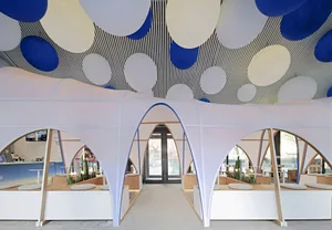 An indoor cafe with modern white fabric-texture walls and ceiling, featuring blue and white circular light fixtures.