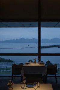 A modern restaurant with floor-to-ceiling windows overlooking a serene waterfront